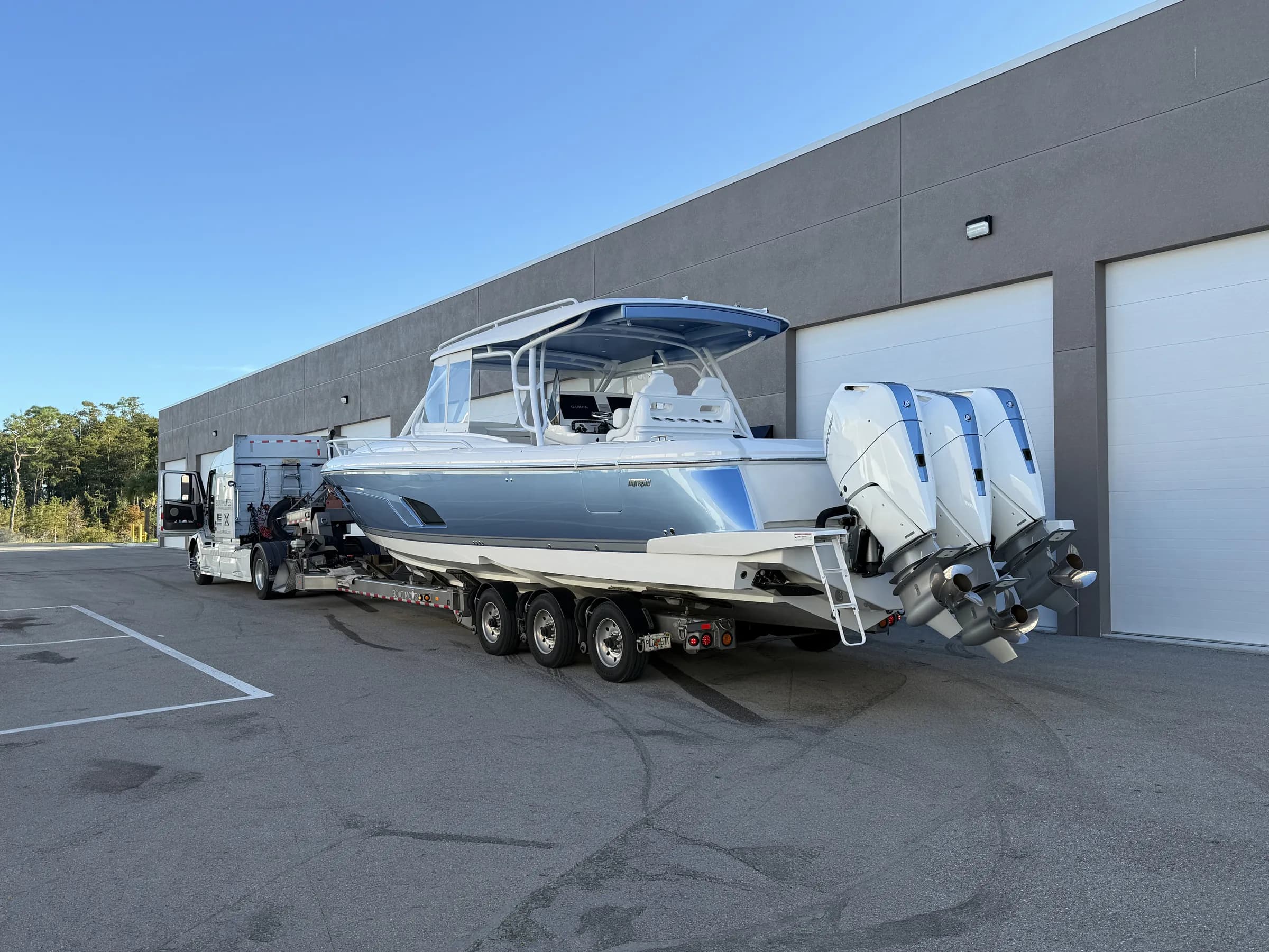 A center-console boat with triple outboards on its trailer outside Vehicle Fortress garage doors